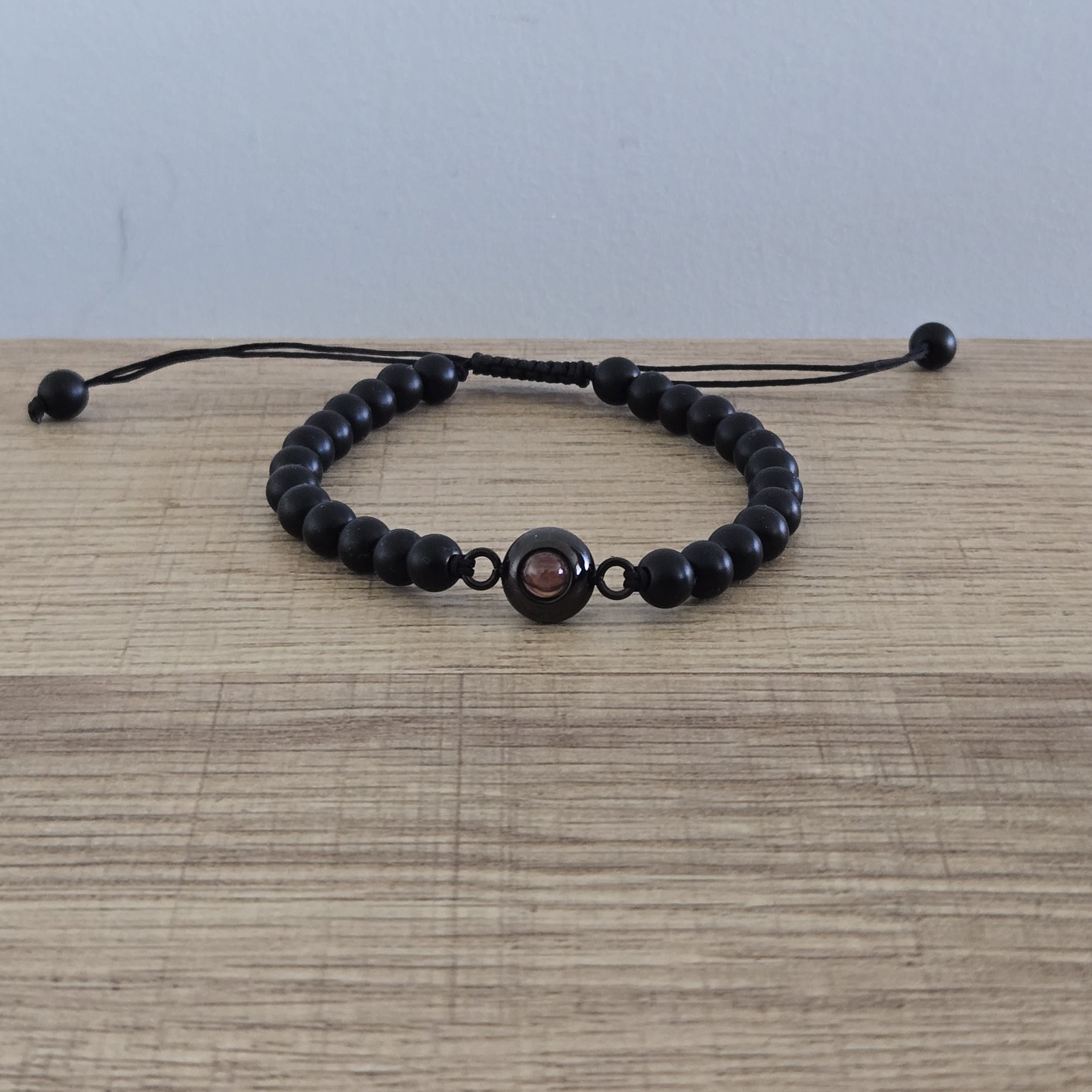 Pulsera de color negro, con cuentas redondas, y una gema al centro que contiene una foto personalizada. 